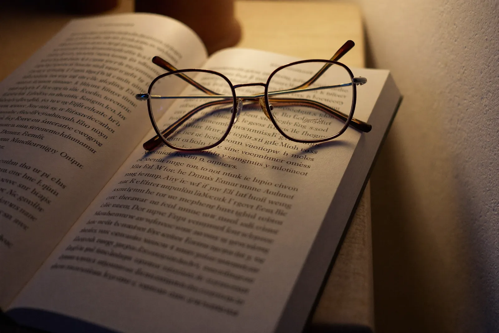 A pair of reading glasses resting on an open paperback in warm lamplight