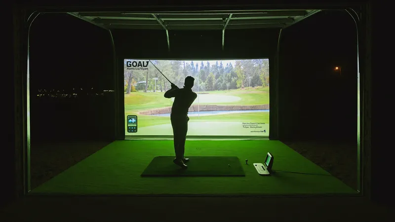 A man mid golf swing in a dark garage, facing a glowing simulator screen showing a fairway