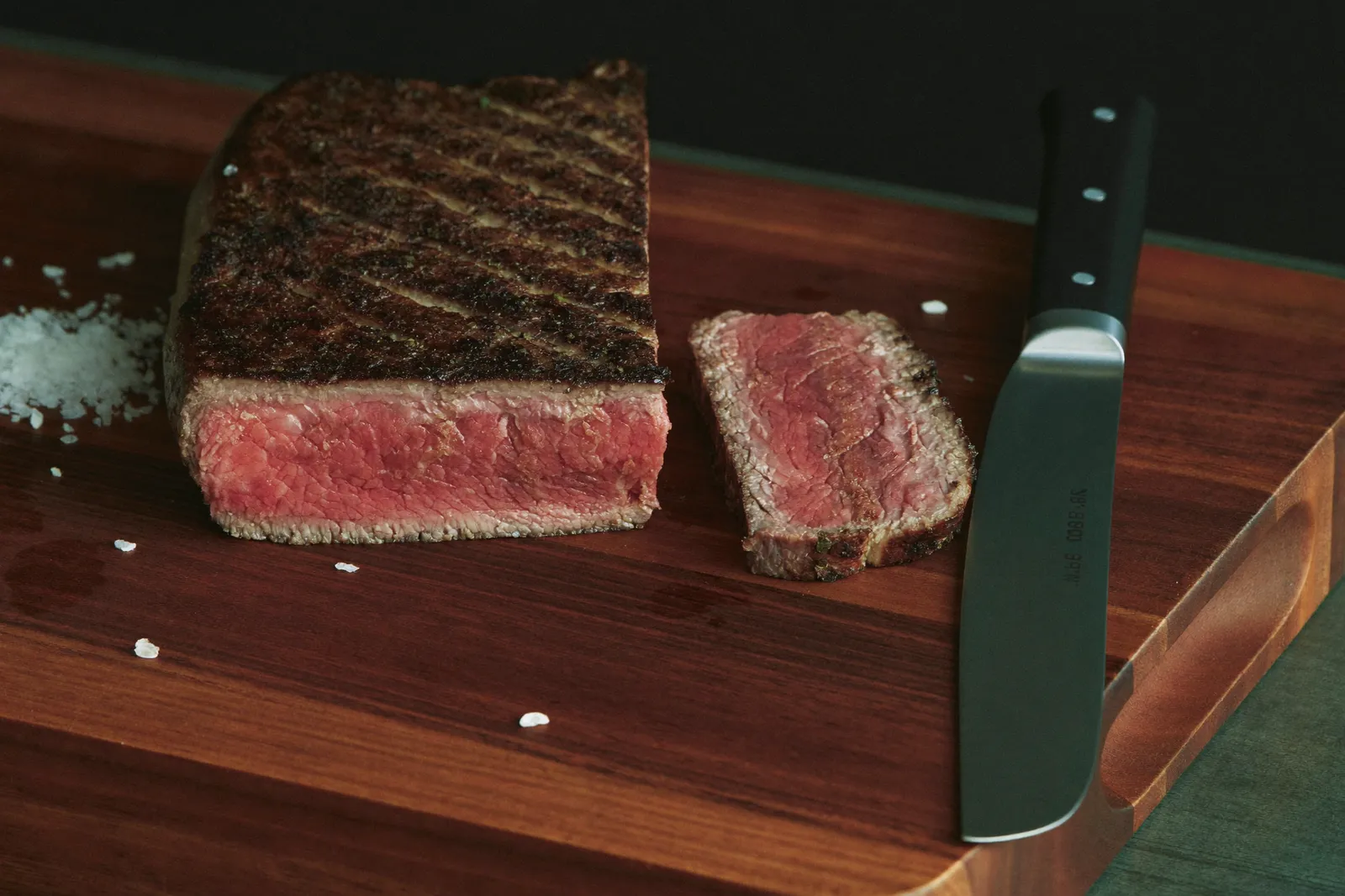 Sliced ribeye steak on a walnut cutting board, rosy from edge to edge with a dark seared crust