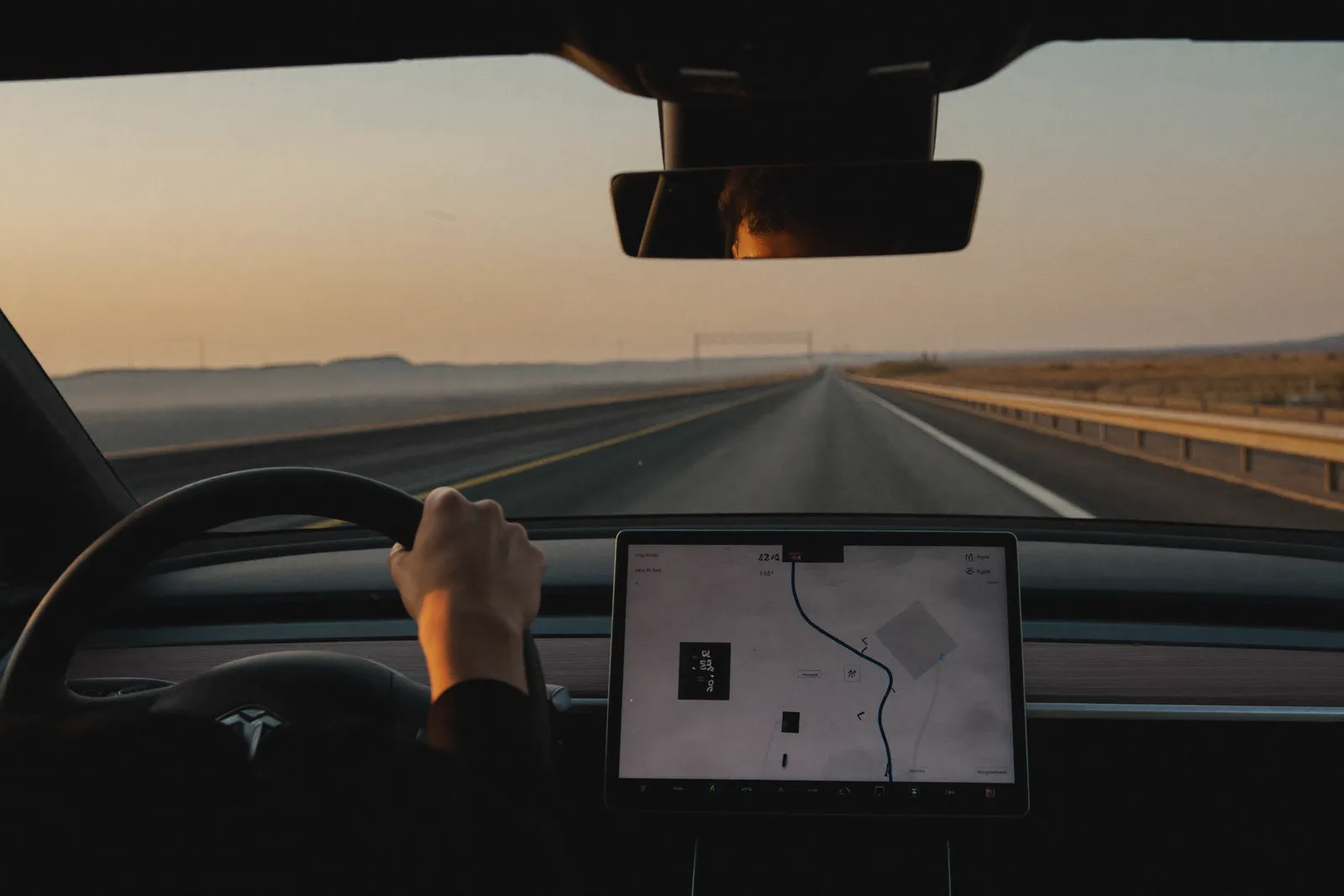 Over the shoulder of a driver at dawn on an empty highway, hands calm on the wheel