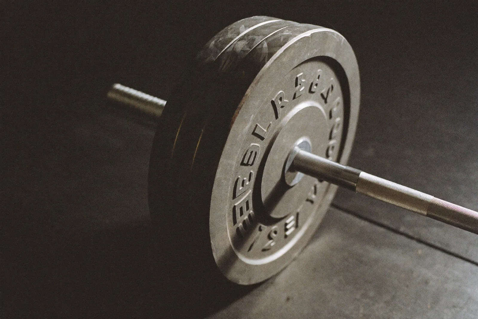 A loaded barbell with steel plates on a home gym platform, chalk on the knurling