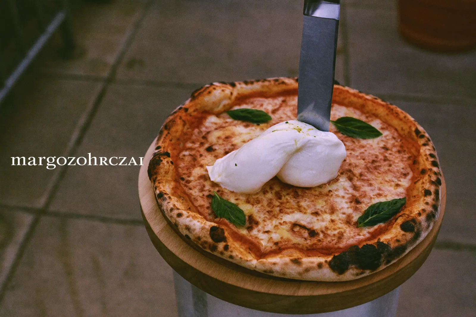 A margherita pizza with a leopard-spotted charred crust on a wooden peel