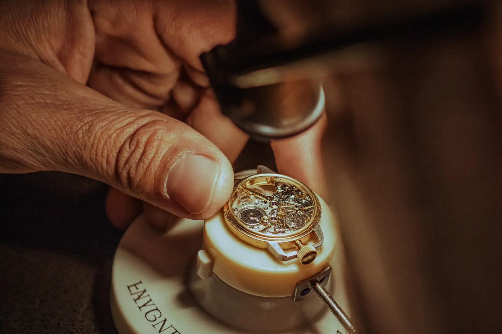 A watchmaker inspecting an open mechanical watch movement through a loupe