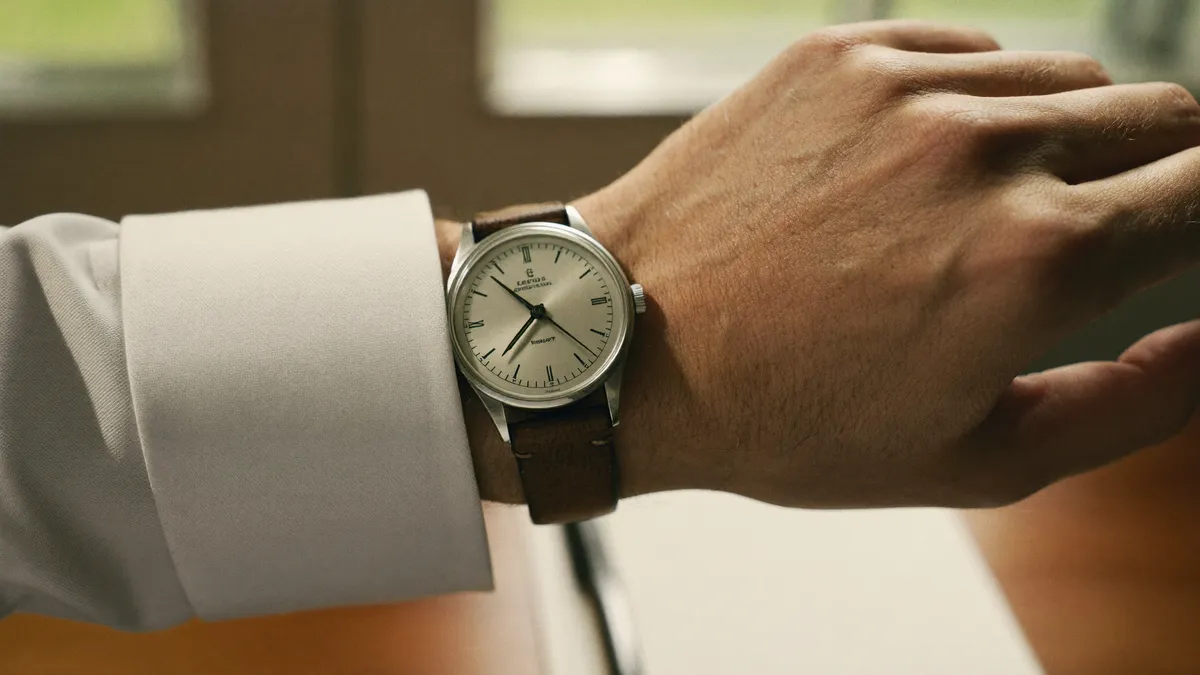 A vintage stainless steel dress watch on a worn leather strap, on a man's wrist below a white oxford cuff