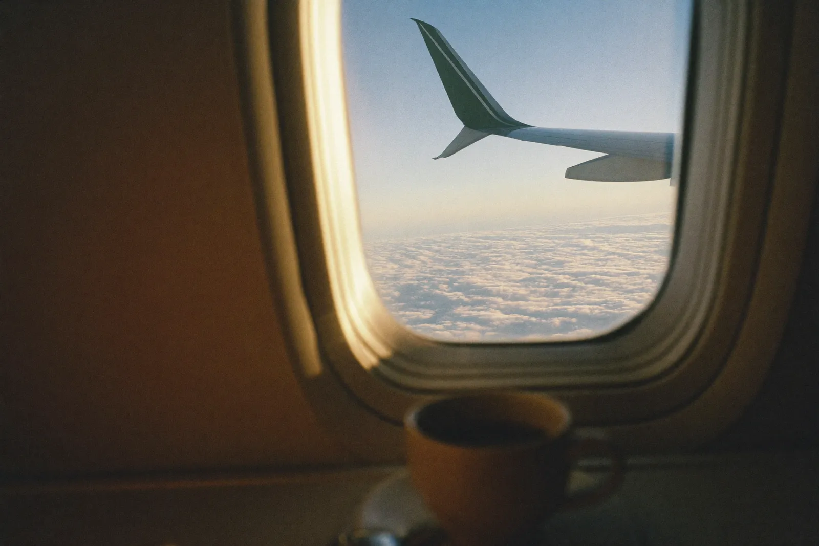 The view over an airplane wing at golden hour, a coffee cup on the tray table in the foreground
