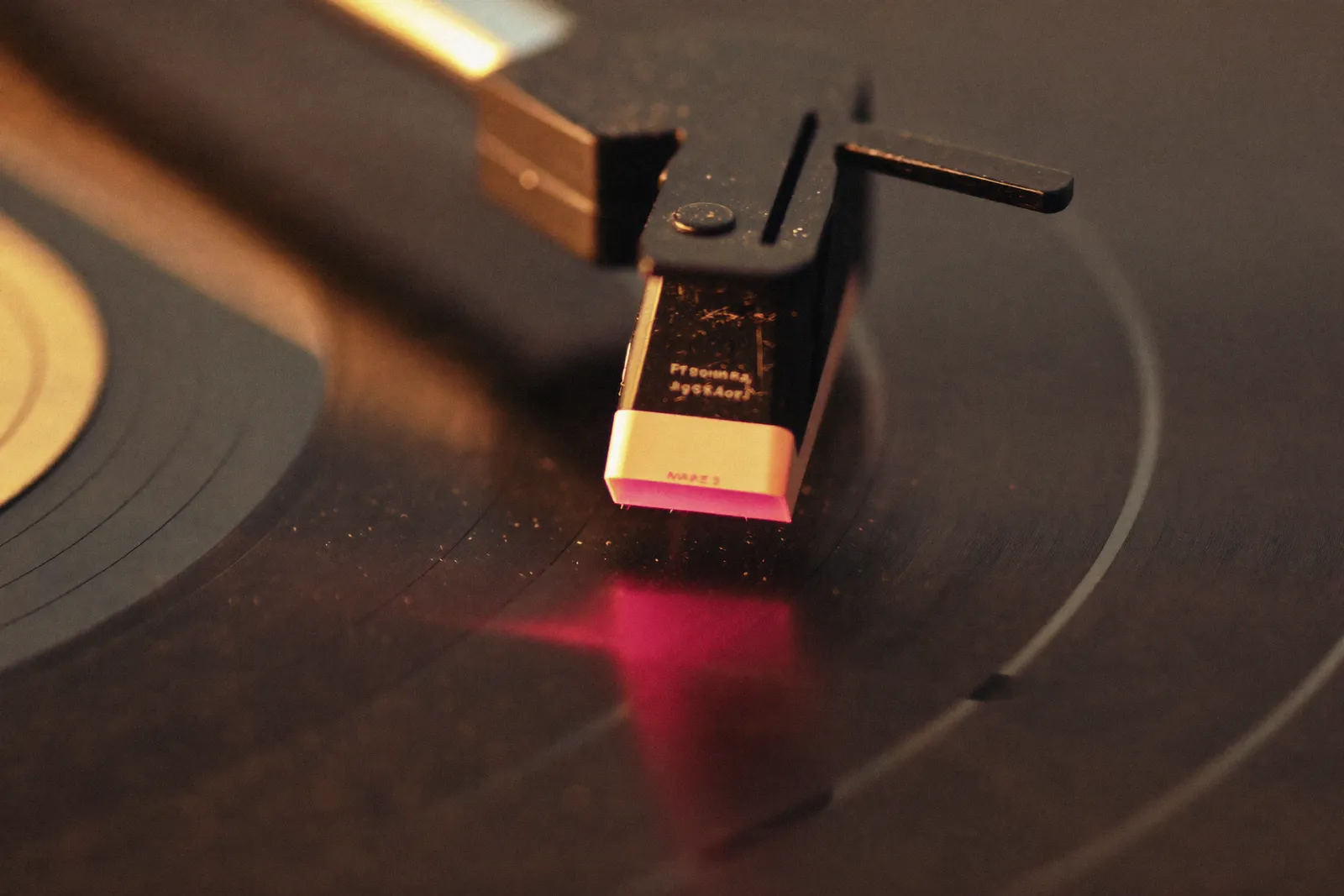 A turntable stylus lowering onto a spinning vinyl record in warm lamplight