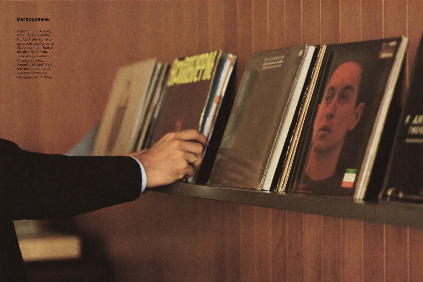 A man's hands flipping through a shelf of vinyl records in a wood-paneled study