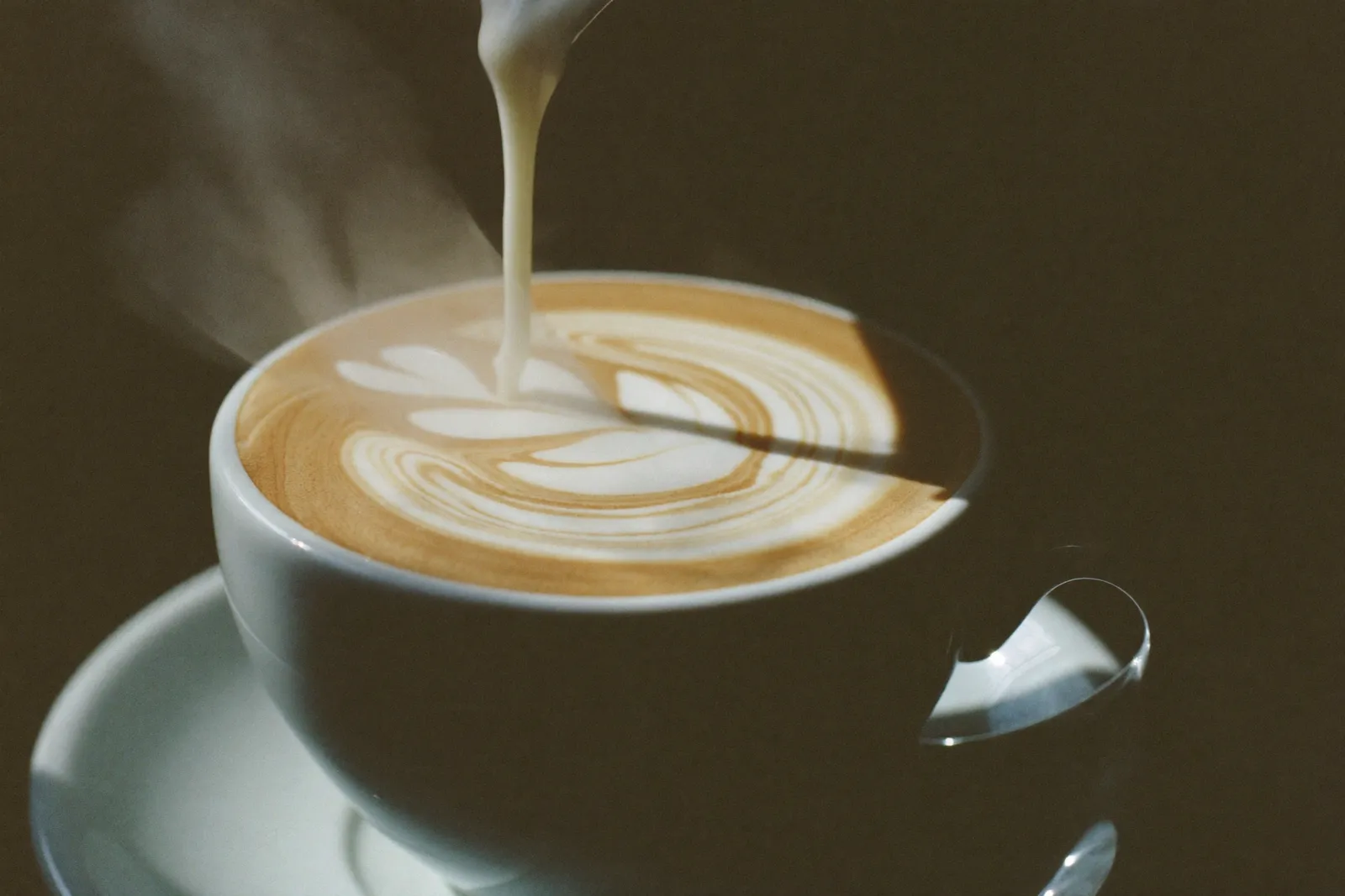Latte art being poured into a white ceramic cup, a rosetta pattern half formed
