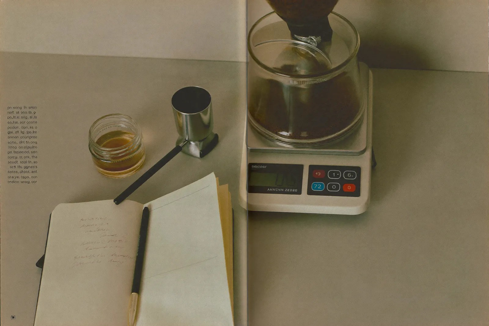 A burr grinder, precision scale, and open notebook of dial-in notes on a kitchen counter